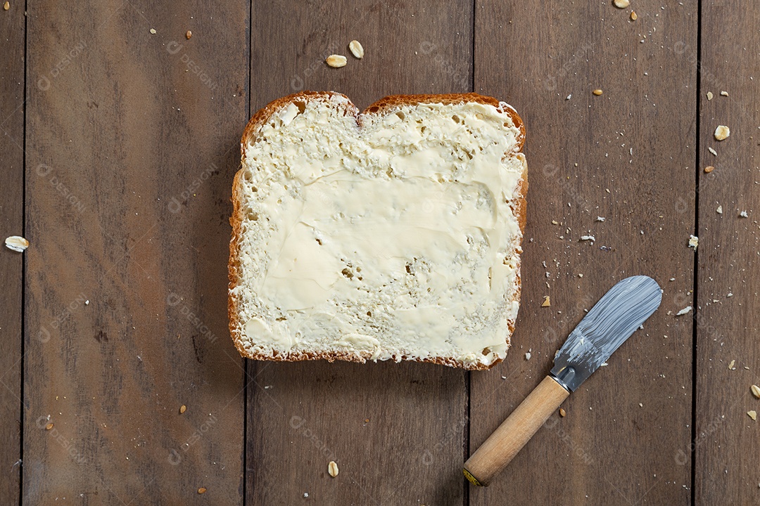 Fatias de pão com margarina em uma mesa de madeira.