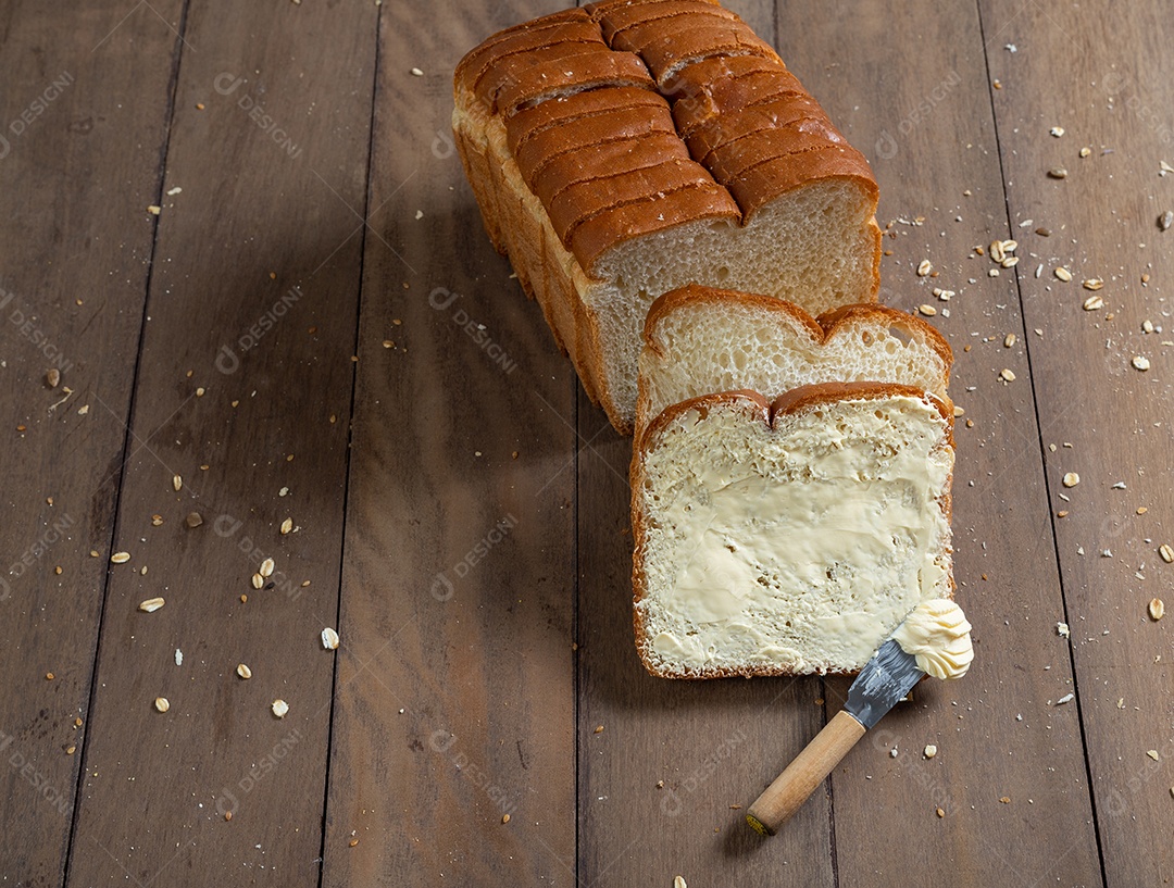 Fatias de pão com margarina em uma mesa de madeira.