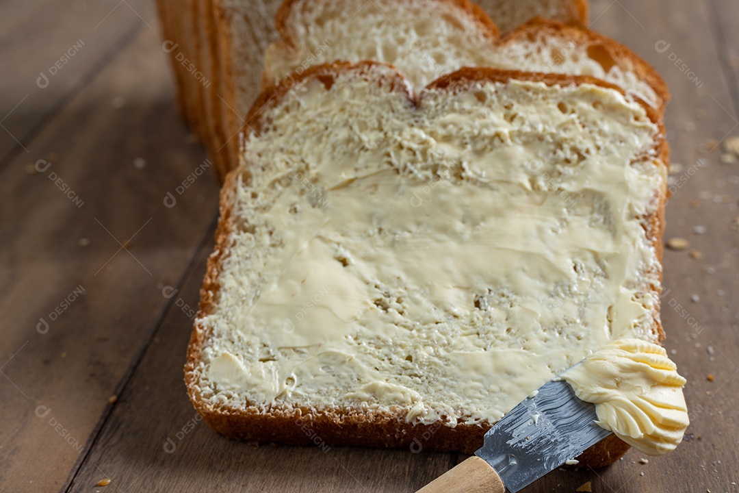 Fatias de pão com margarina em uma mesa de madeira.