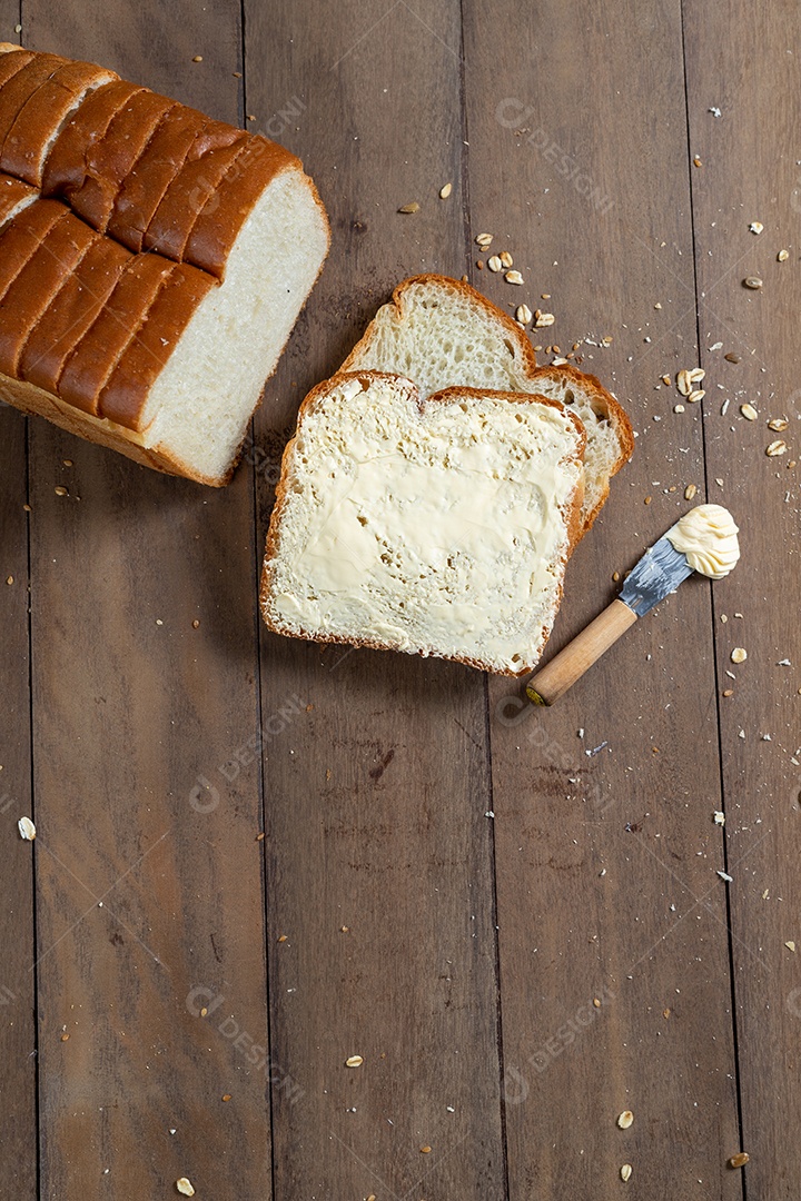 Fatias de pão com margarina em uma mesa de madeira.