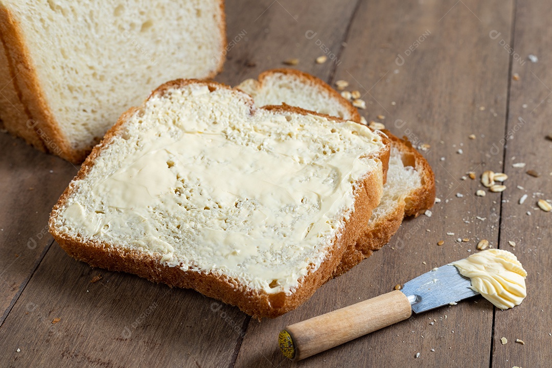 Fatias de pão com margarina em uma mesa de madeira.