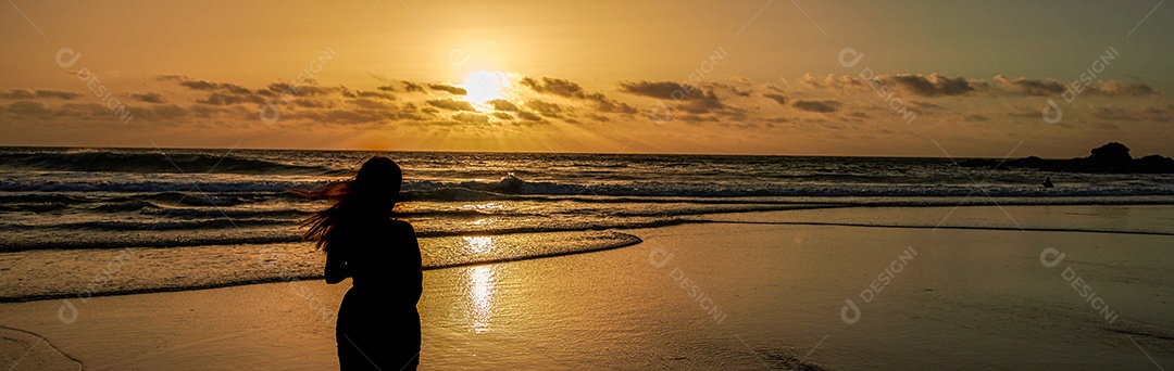 Silhueta de uma jovem assistindo o pôr do sol na praia, desfrutando da liberdade e da vida - conceito de bem-estar de viagens de pessoas