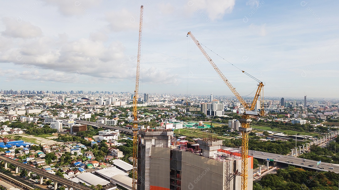 Grande canteiro de obras, incluindo vários guindastes trabalhando em um complexo de construção, com céu azul claro e sol