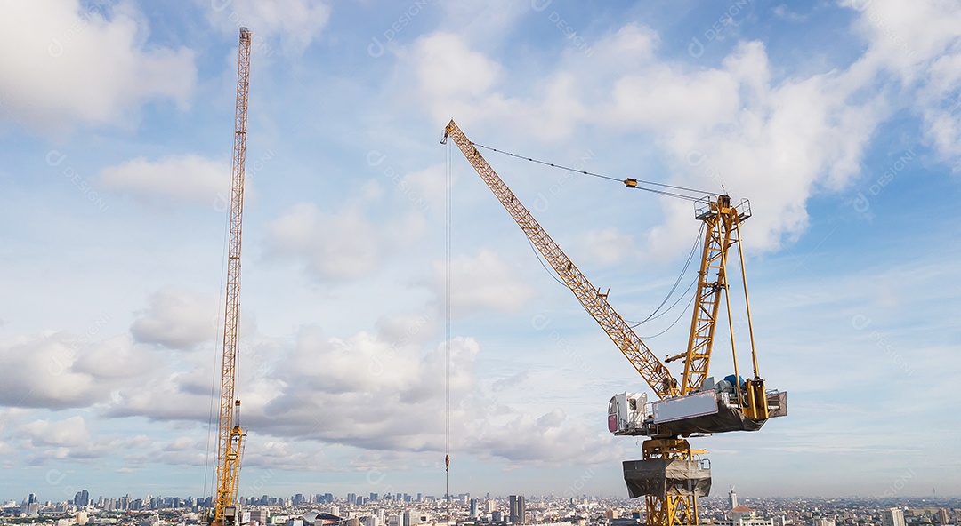 Grande canteiro de obras, incluindo vários guindastes trabalhando em um complexo de construção, com céu azul claro e sol