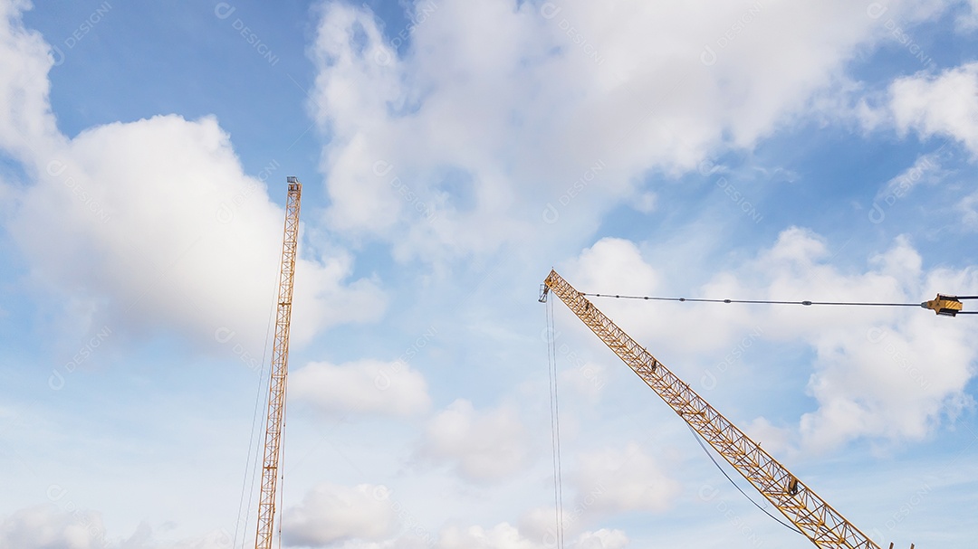 Grande canteiro de obras, incluindo vários guindastes trabalhando em um complexo de construção, com céu azul claro e sol