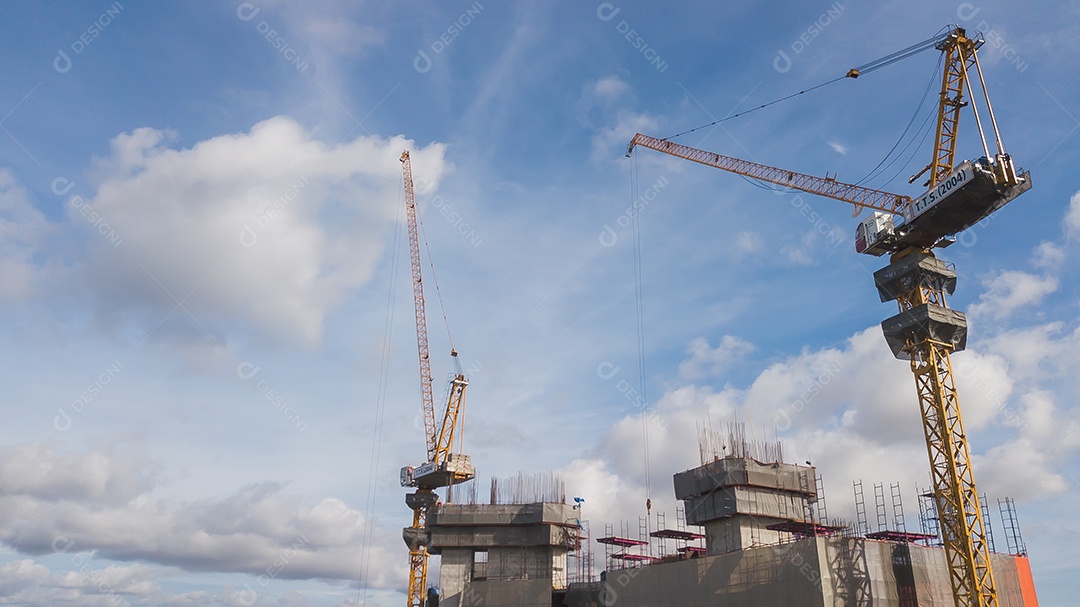 Grande canteiro de obras, incluindo vários guindastes trabalhando em um complexo de construção, com céu azul claro e sol