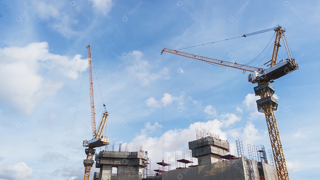 Grande canteiro de obras, incluindo vários guindastes trabalhando em um complexo de construção, com céu azul claro e sol
