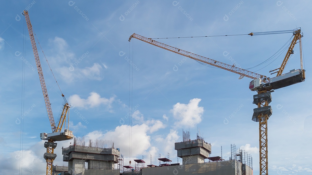 Grande canteiro de obras, incluindo vários guindastes trabalhando em um complexo de construção, com céu azul claro e sol