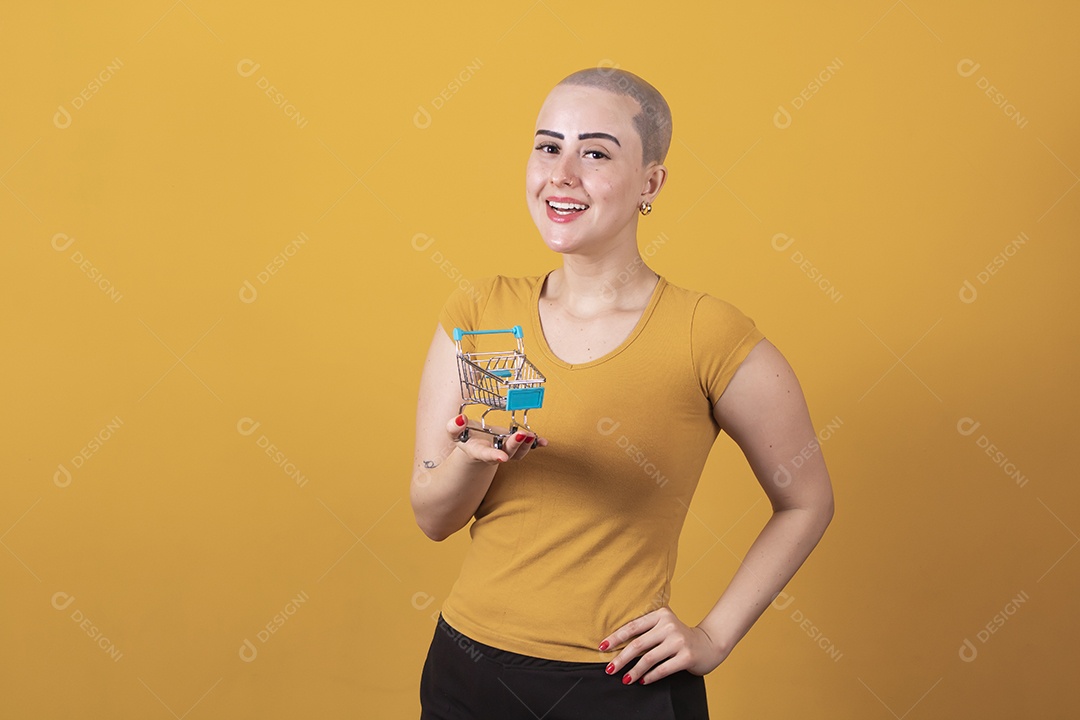 Linda mulher jovem careca segurando um carrinho de compras, conceito outubro rosa