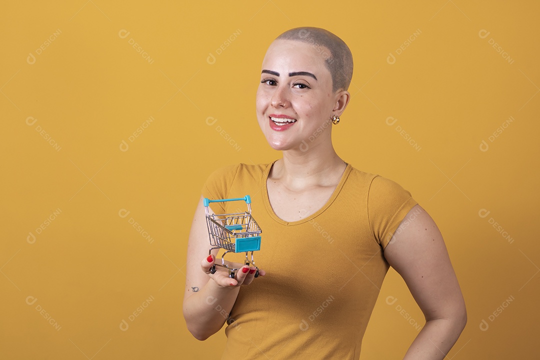 Linda mulher jovem careca segurando um carrinho de compras, conceito outubro rosa