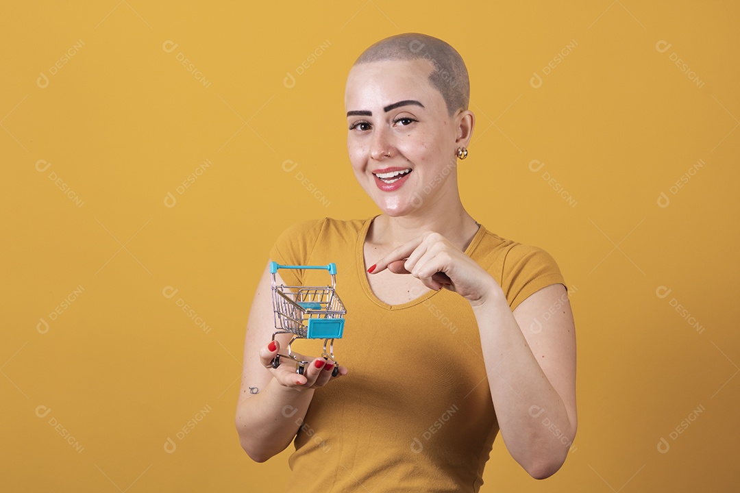 Linda mulher jovem careca segurando um carrinho de compras, conceito outubro rosa