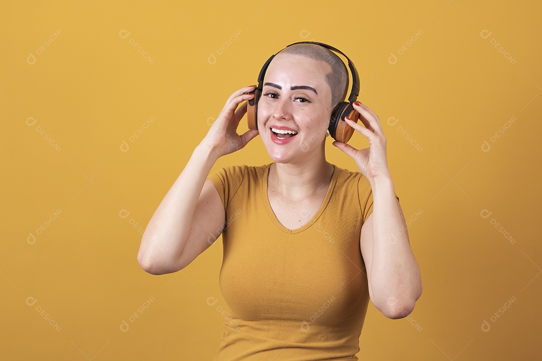 Mulher jovem careca usando blusa bege com fone de ouvido em conceito de câncer, outubro rosa
