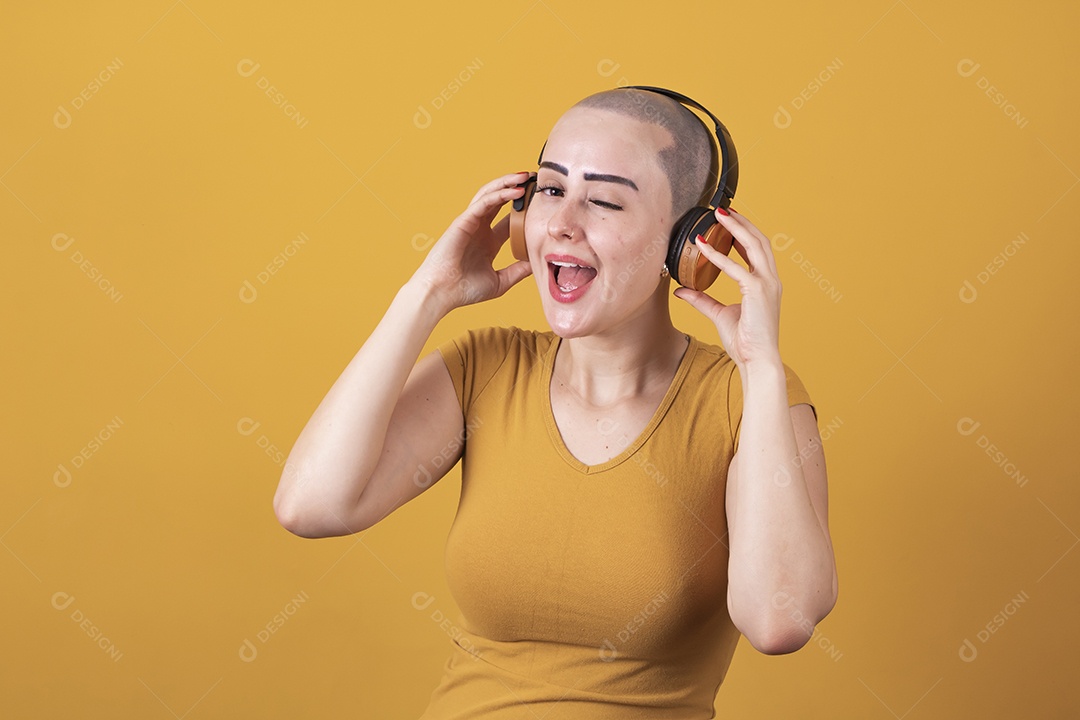 Mulher jovem careca usando blusa bege com fone de ouvido em conceito de câncer, outubro rosa