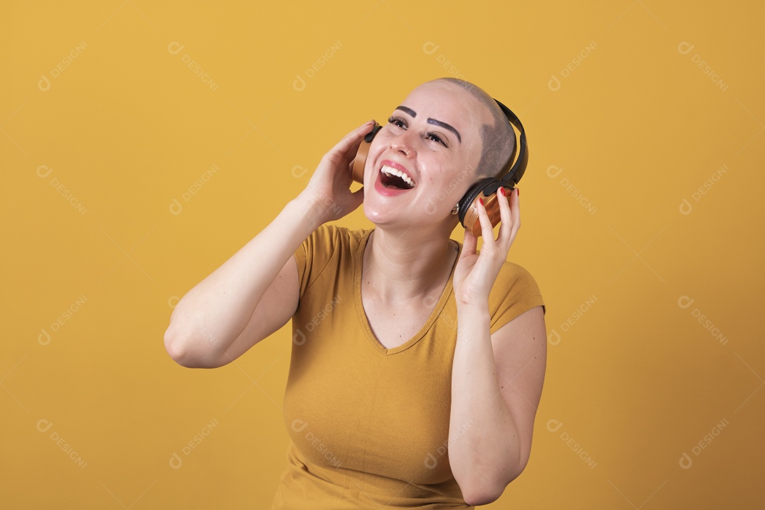 Mulher jovem careca usando blusa bege com fone de ouvido em conceito de câncer, outubro rosa