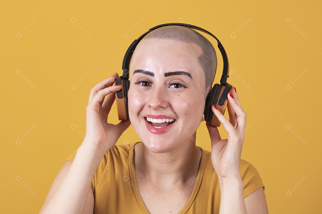 Mulher jovem careca usando blusa bege com fone de ouvido em conceito de câncer, outubro rosa