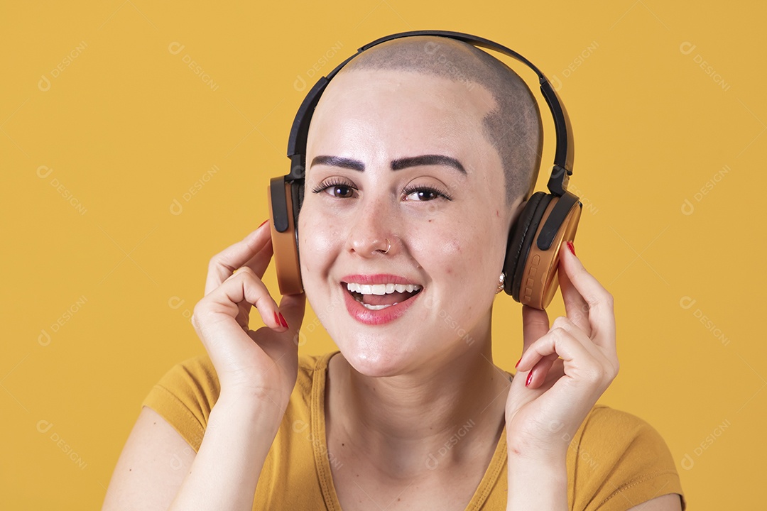 Mulher jovem careca usando blusa bege com fone de ouvido em conceito de câncer, outubro rosa