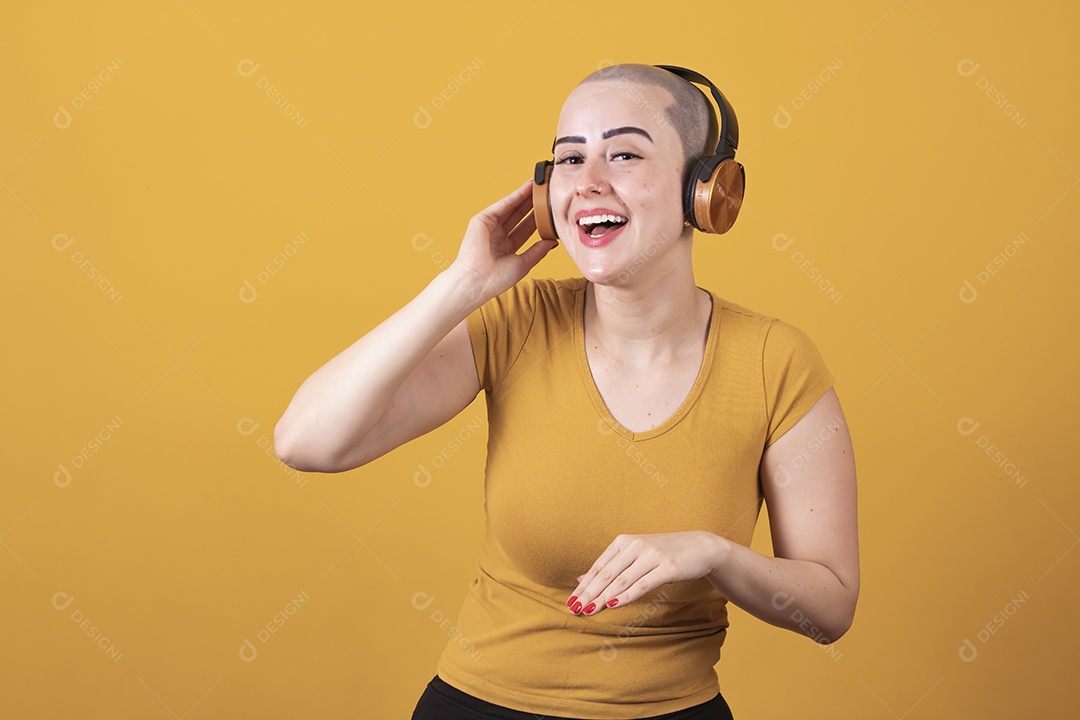 Mulher jovem careca usando blusa bege com fone de ouvido em conceito de câncer, outubro rosa