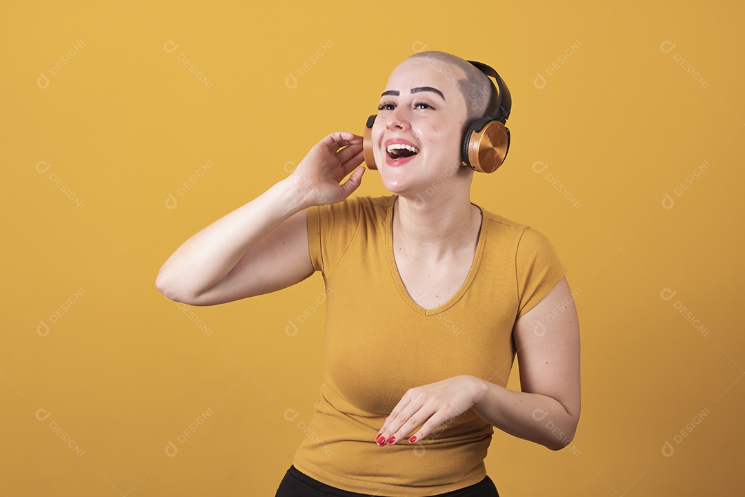 Mulher jovem careca usando blusa bege com fone de ouvido em conceito de câncer, outubro rosa