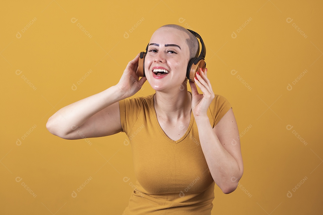 Mulher jovem careca usando blusa bege com fone de ouvido em conceito de câncer, outubro rosa