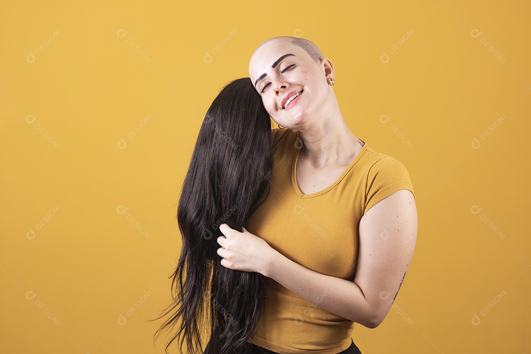 Mulher jovem careca usando blusa bege segurando uma peruca em conceito de câncer, outubro rosa