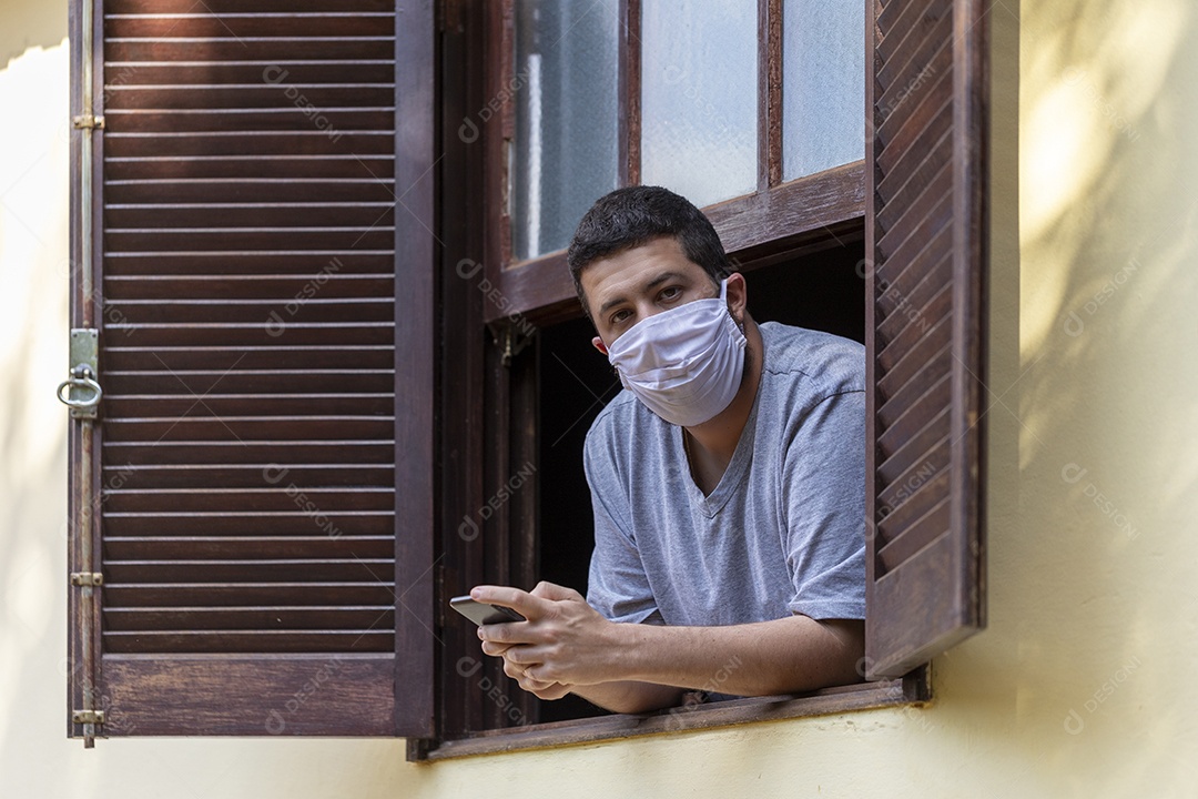 Homem jovem usando mascara mexendo em seu celular