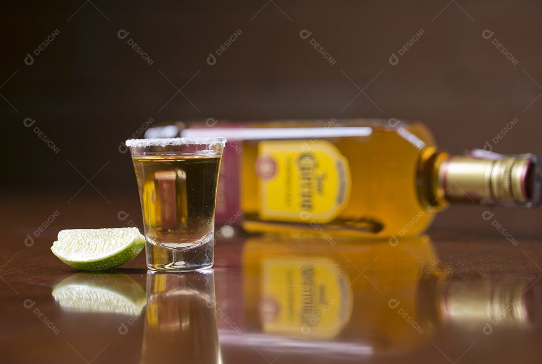 Dose de bebida alcoólica e fatia de limão sobre mesa de madeira