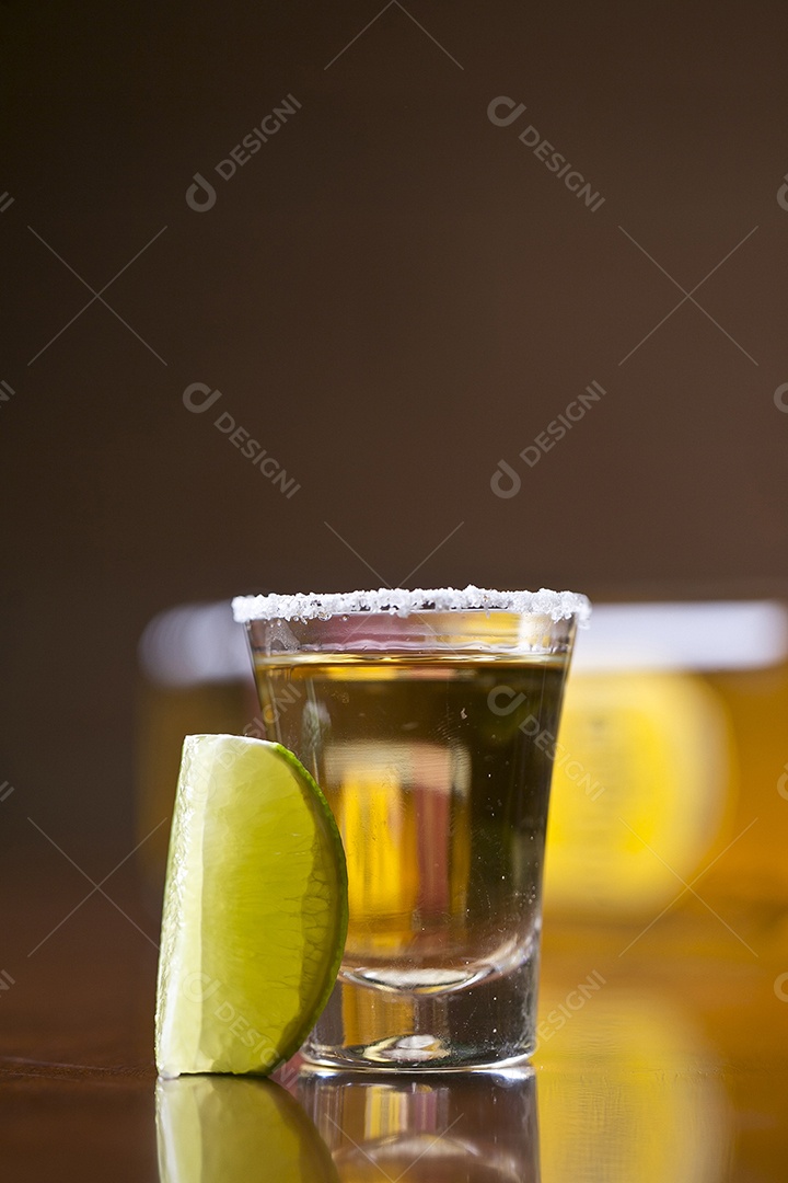 Dose de bebida alcoólica e fatia de limão sobre mesa de madeira