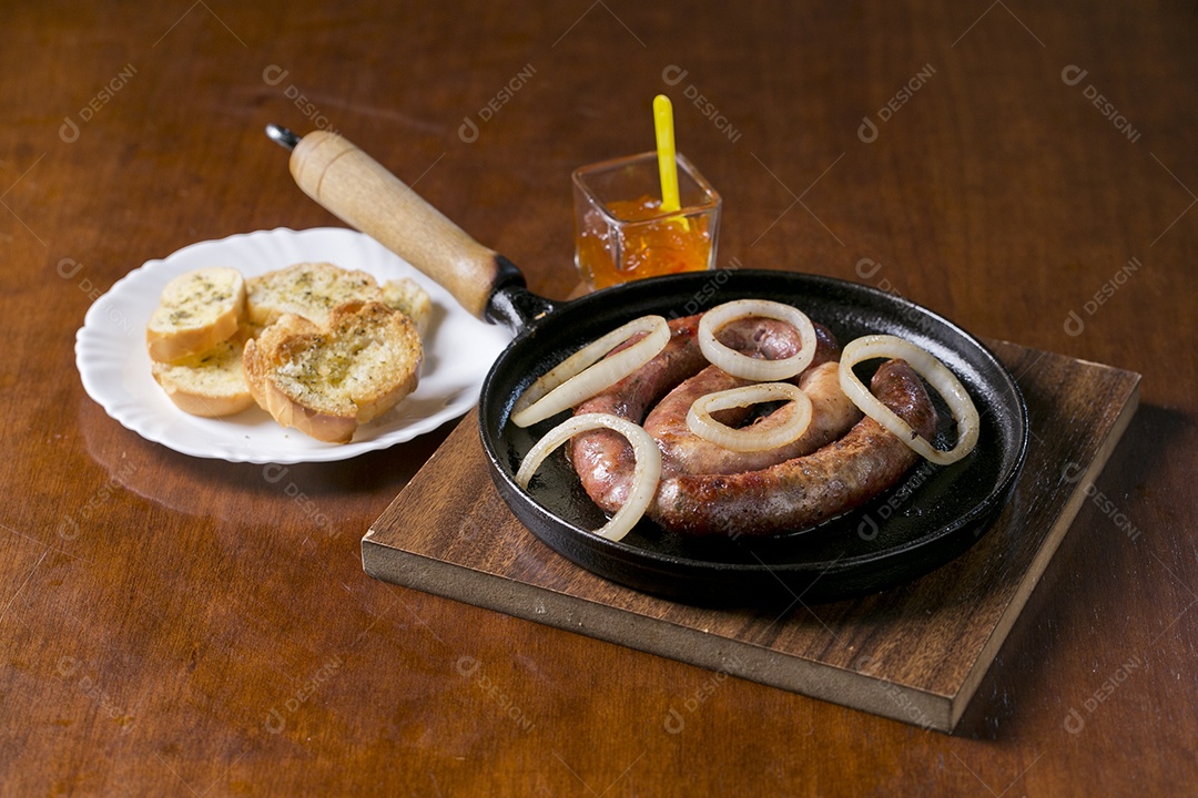 Panela com linguiça frita acebolada e torradas sobre a mesa