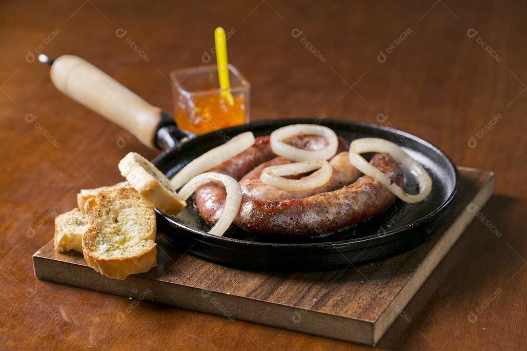 Panela com linguiça frita acebolada e torradas sobre a mesa