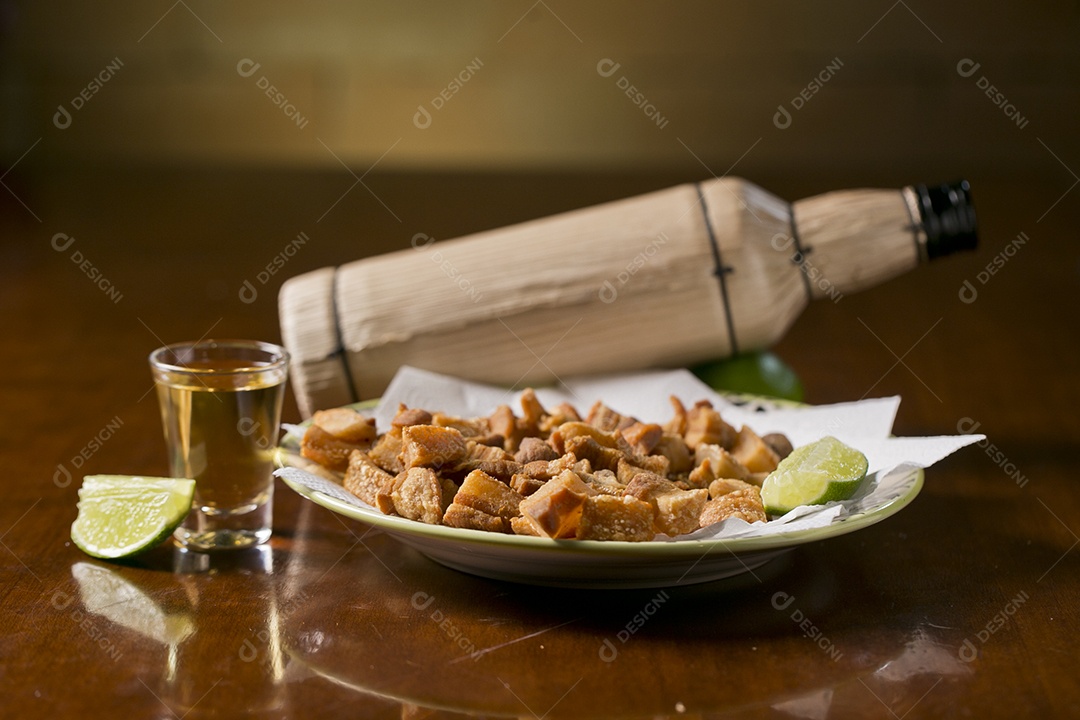 Porção de torresmo frito e copo de tequila sobre a mesa