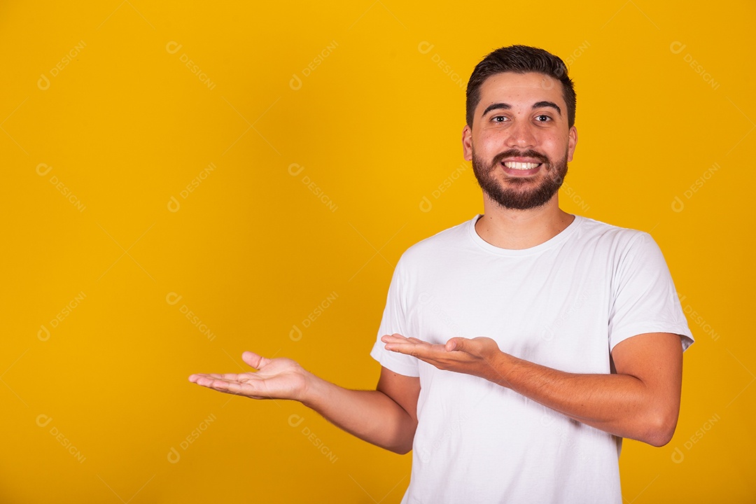 Homem jovem brasileiro sorridente barbudo apontando para lado fundo amarelo