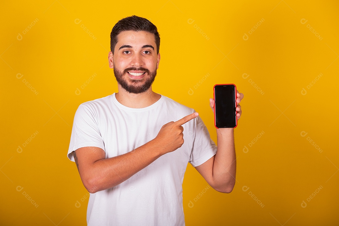 Homem jovem brasileiro segurando celular smartphone fundo amarelo