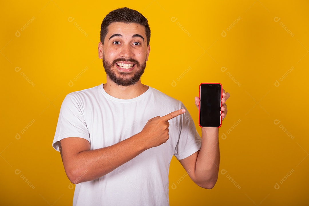 Homem jovem brasileiro segurando celular smartphone fundo amarelo