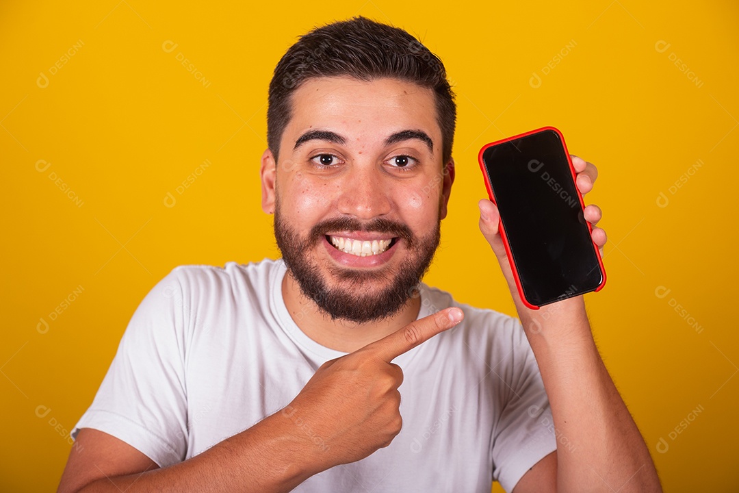 Homem jovem brasileiro segurando celular smartphone fundo amarelo