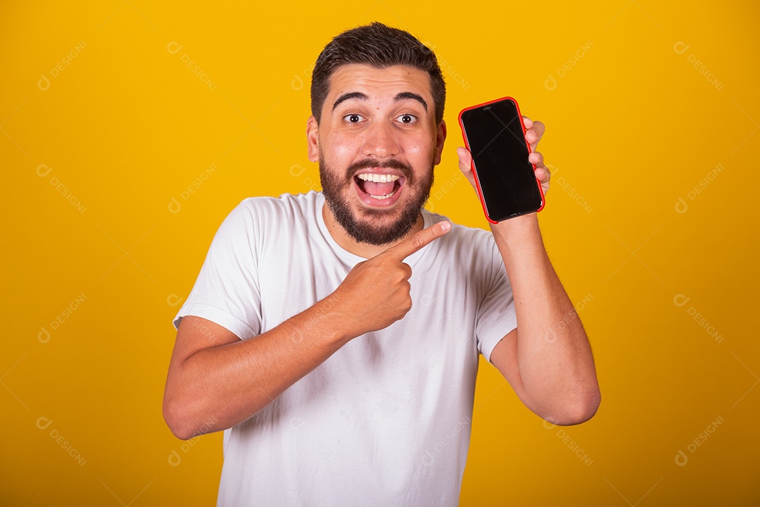 Homem jovem brasileiro segurando celular smartphone fundo amarelo