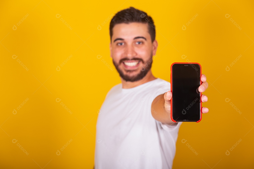 Homem jovem brasileiro segurando celular smartphone fundo amarelo