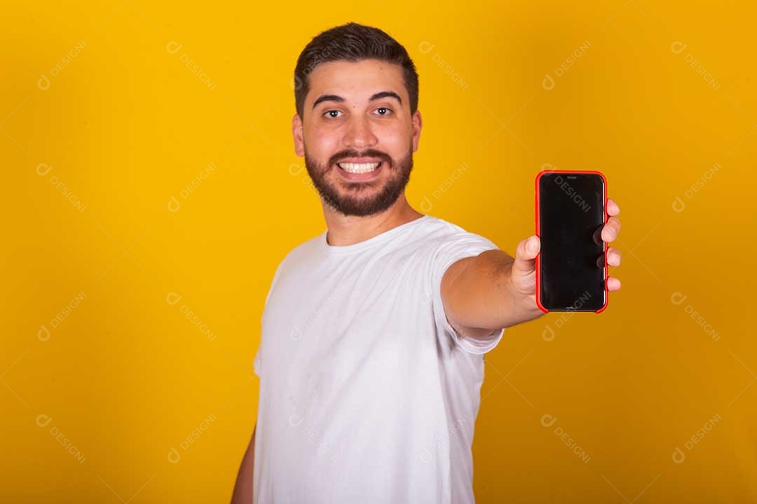 Homem jovem brasileiro segurando celular smartphone fundo amarelo