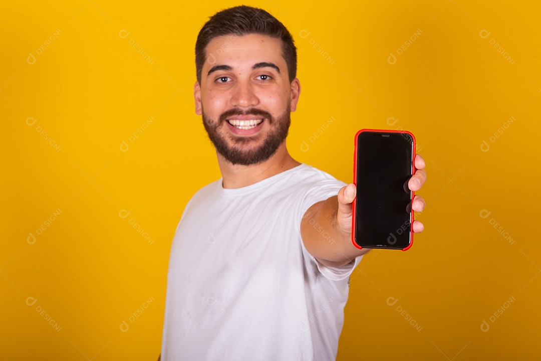 Homem jovem brasileiro segurando celular smartphone fundo amarelo
