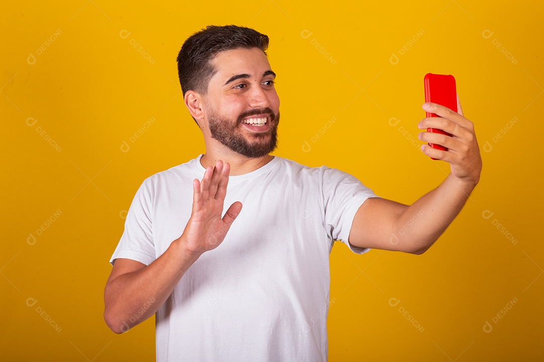 Homem jovem brasileiro segurando celular smartphone fundo amarelo
