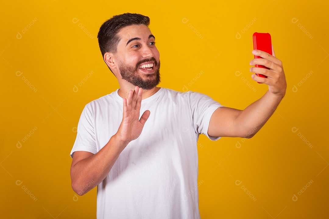 Homem jovem brasileiro segurando celular smartphone fundo amarelo