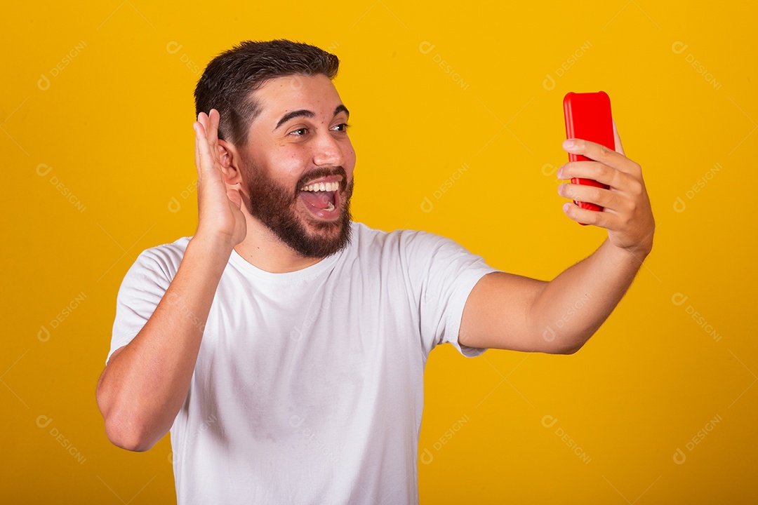 Homem jovem brasileiro segurando celular smartphone fundo amarelo