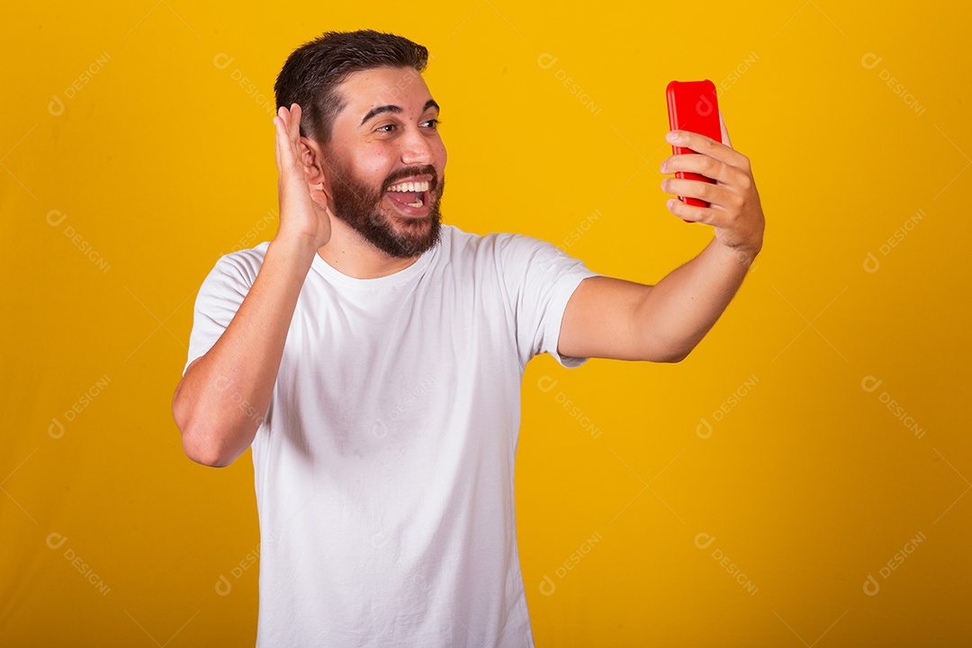 Homem jovem brasileiro segurando celular smartphone fundo amarelo