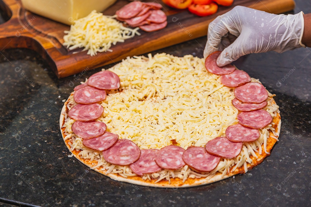 Preparação de pizza, espalhando rodelas de pepperoni e fatias na pizza