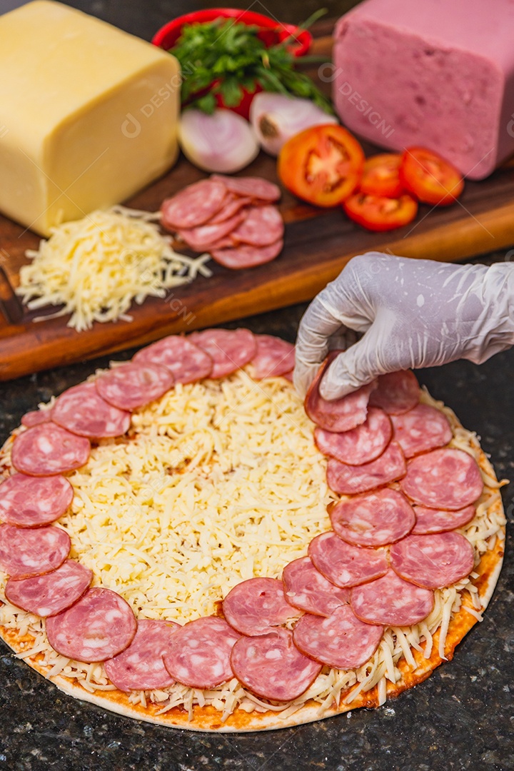 Preparação de pizza, espalhando rodelas de pepperoni e fatias na pizza