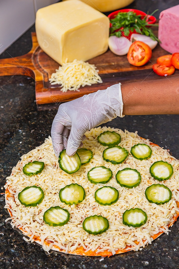 Preparação de pizza, espalhando fatias de pepino e fatias em vegetais