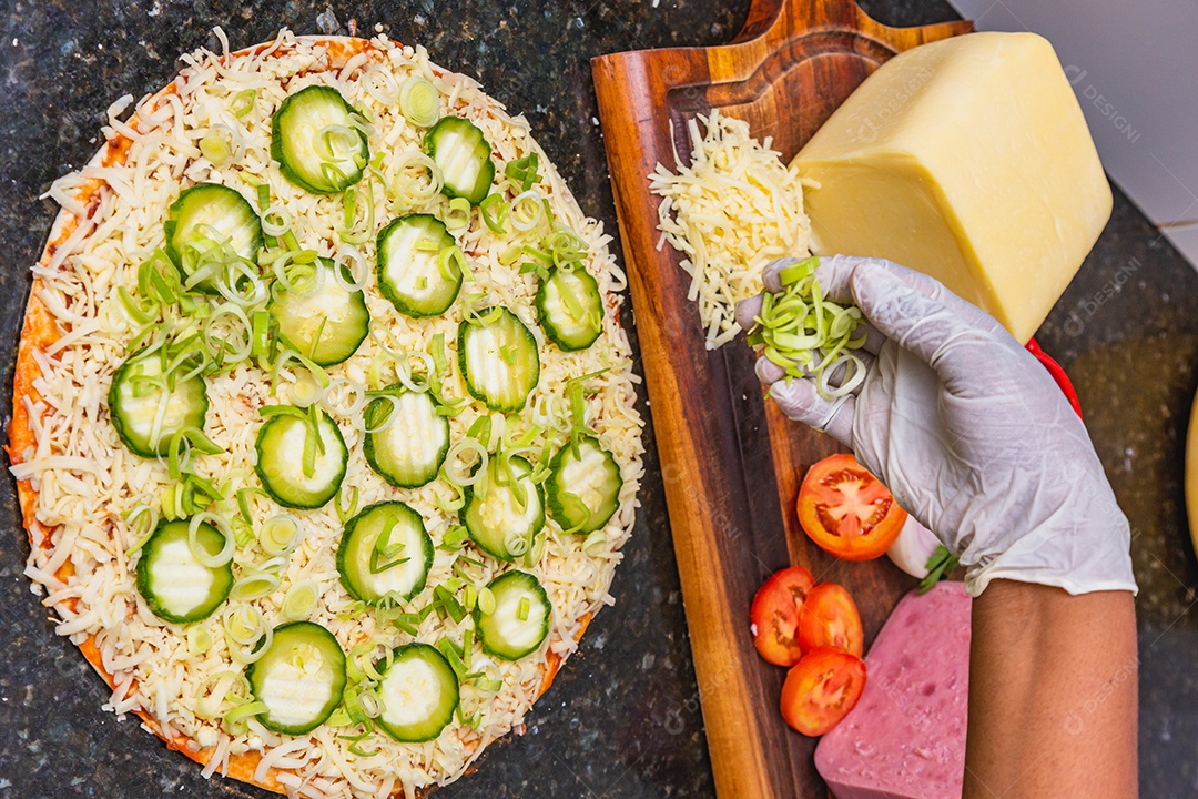 Preparação de pizza, espalhando fatias de pepino e fatias em vegetais
