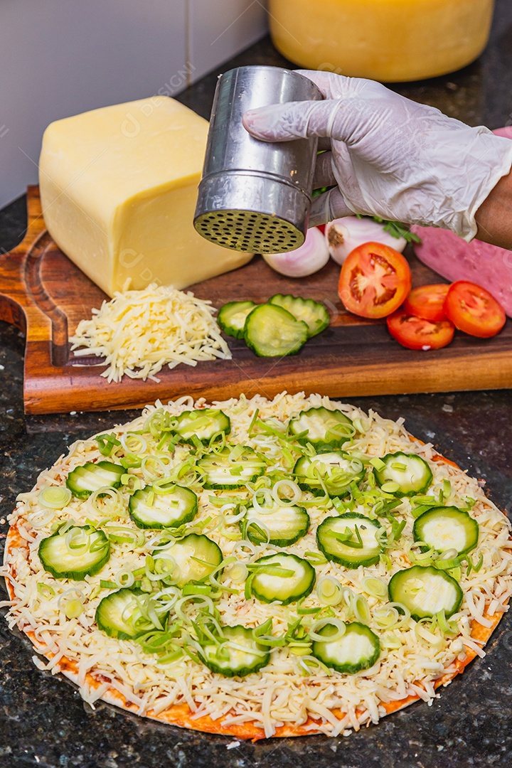 Preparação de pizza, espalhando fatias de pepino e fatias em vegetais