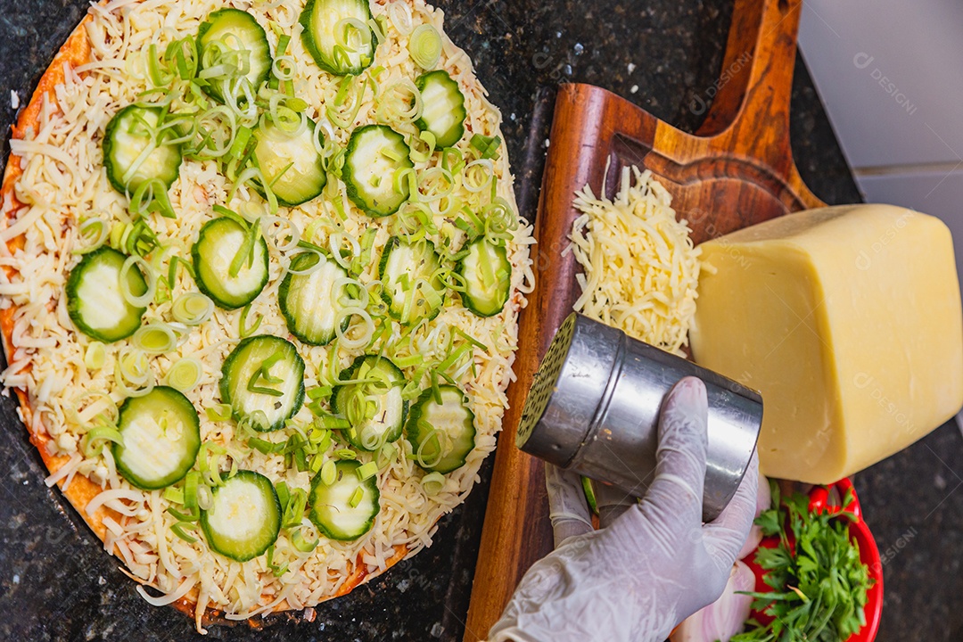 Preparação de pizza, espalhando fatias de pepino e fatias em vegetais