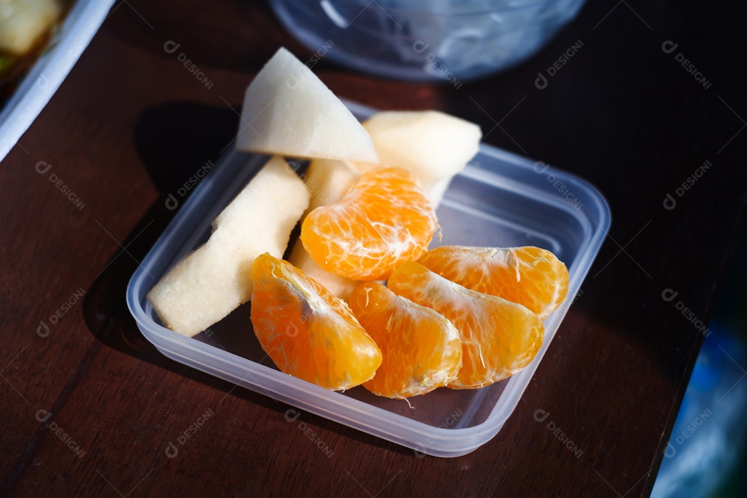 Fatia de tangerina e maçã no prato transparente sobre a mesa de madeira