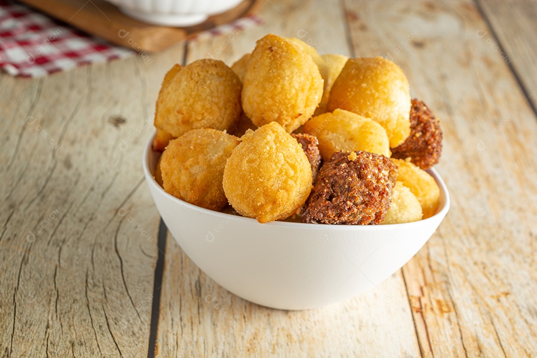 Salgadinhos de festa brasileiros, mistura de petiscos de festa tradicional com coxinha, kibe e outros petiscos fritos sobre mesa de madeira em um recipiente branco.